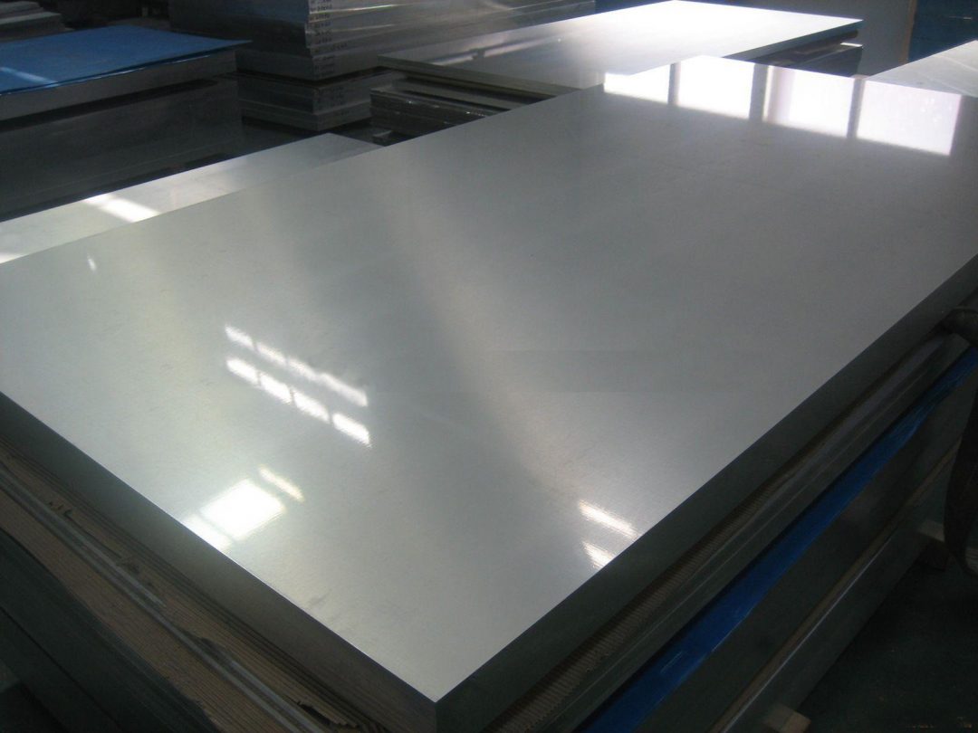 Plat stainless steel 304 dengan tekstur brushed yang halus, memantulkan cahaya lembut di sekitarnya.